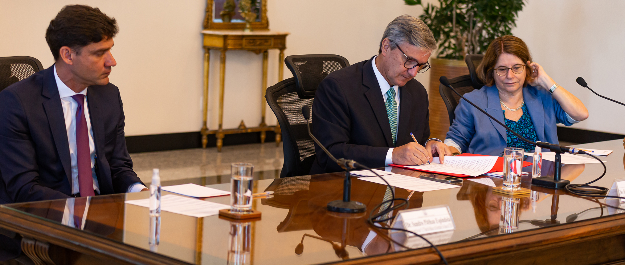 Presidente desembargador Henrique Figueira assina termo de colaboração com Instituto Dara em mesa, sentado entre o juiz Sandro Espindola e a médica Vera Cordeiro