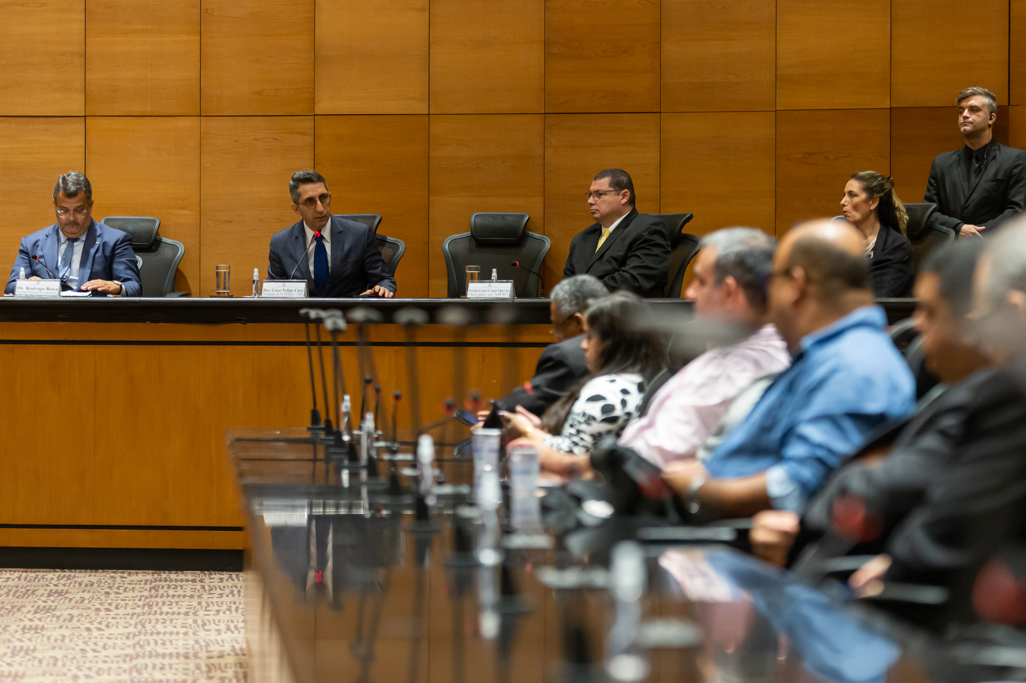 Em destaque desembargador César Cury com plateia desfocada acompanhando 