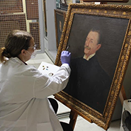 Fotografia de uma restauradora trabalhando na restauração do quadro do desembargador Antônio Soares de Pinto Junior